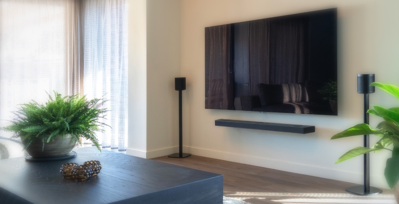 A television on the wall with two speakers next to it on speaker stands in the living room.