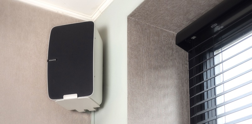 A white speaker is mounted on the wall next to the window by means of a speaker bracket.