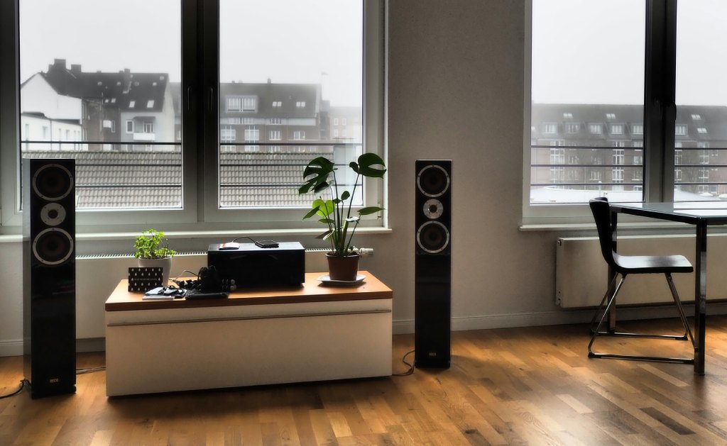 A modern living room with large floor-standing speakers, a low cabinet with plants and a city view.